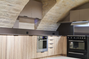 Les meubles sur-mesure, les plans et crédences en quartz et l'électroménager ont pris place. Les tuyauteries d'alimentation existantes, des radiateurs en fonte, les poignées, l'appareillage électrique et les luminaires ont été choisis noirs pour contraster avec les tons chauds de la pierre et des meubles.